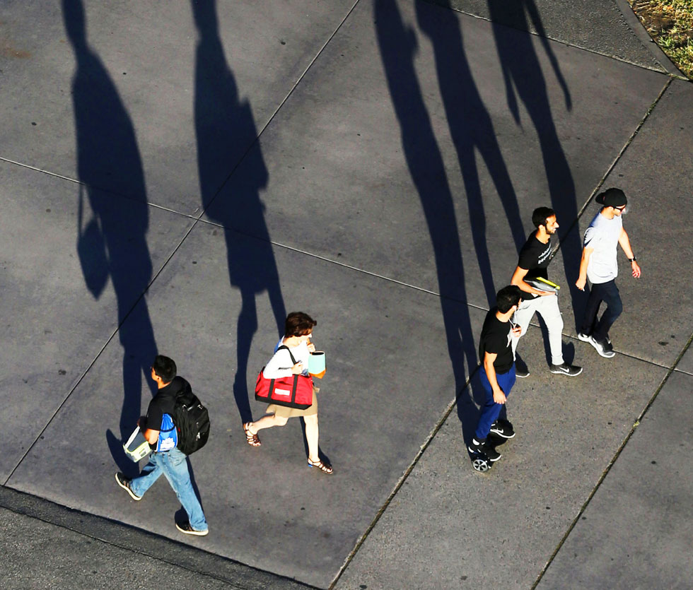Group walks down main campus walkway casting tall shadows along the way Group walks down main campus walkway casting tall shadows along the way