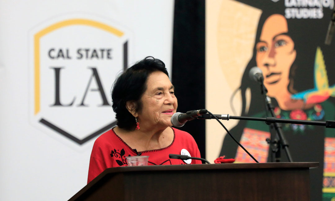 Dolores Huerta speaking in front of a podium at Cal State LA Dolores Huerta speaking in front of a podium at Cal State LA