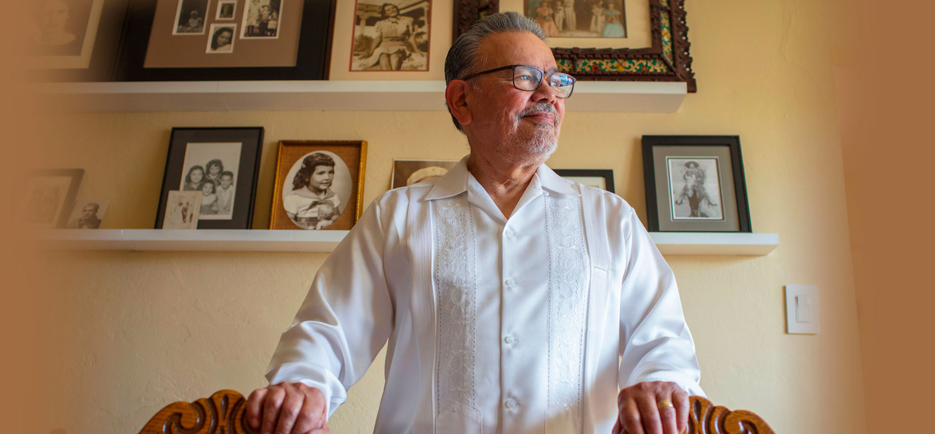 Carlos Munoz Jr. standing in front of a wall of picture frames of his family.