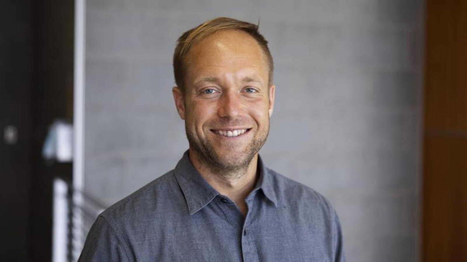 Cal State LA professor J. Bachman smiles in a portrait taken on campus, wearing a gray shirt against a blurred indoor background.