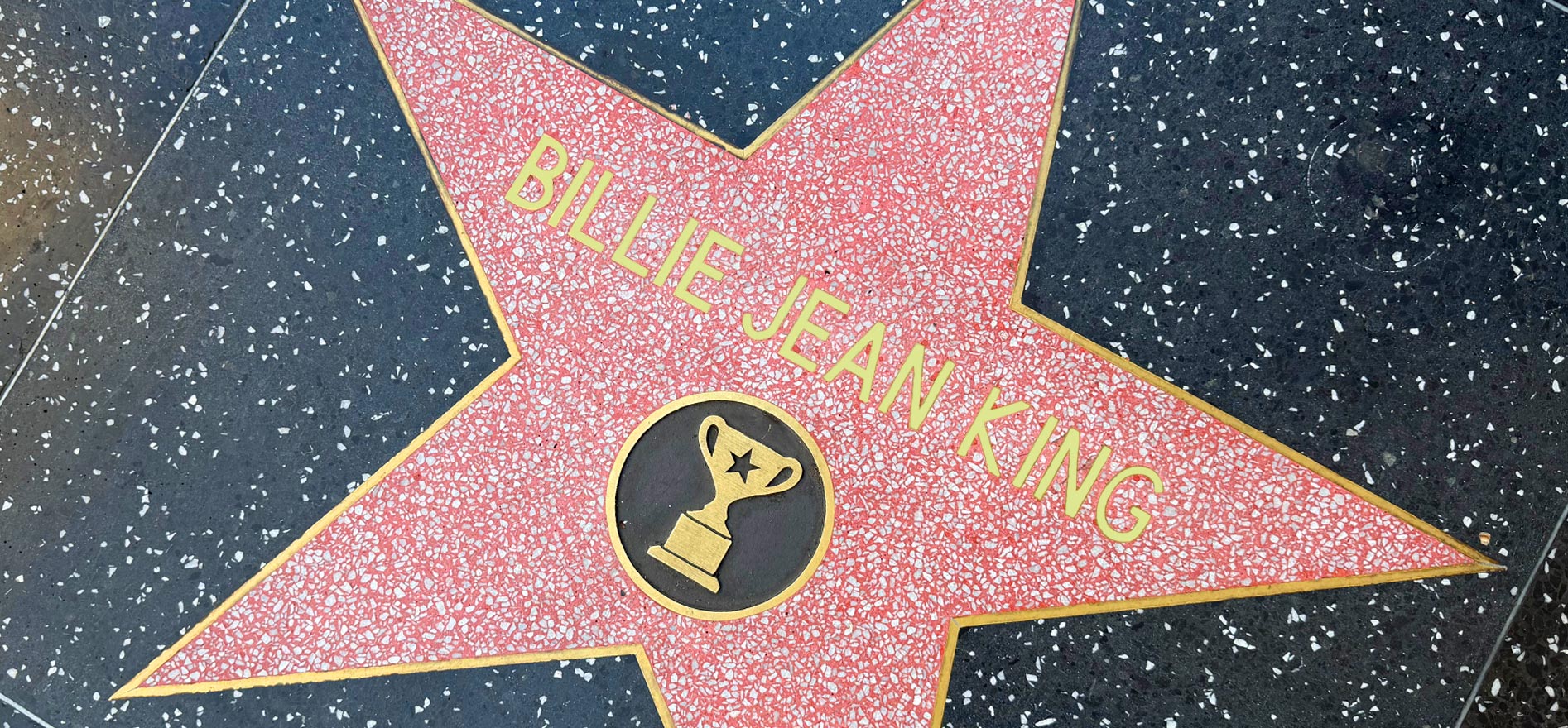 The Hollywood Walk of Fame star honoring tennis legend Billie Jean King, featuring a gold trophy icon set in a pink terrazzo star on a black-speckled sidewalk.