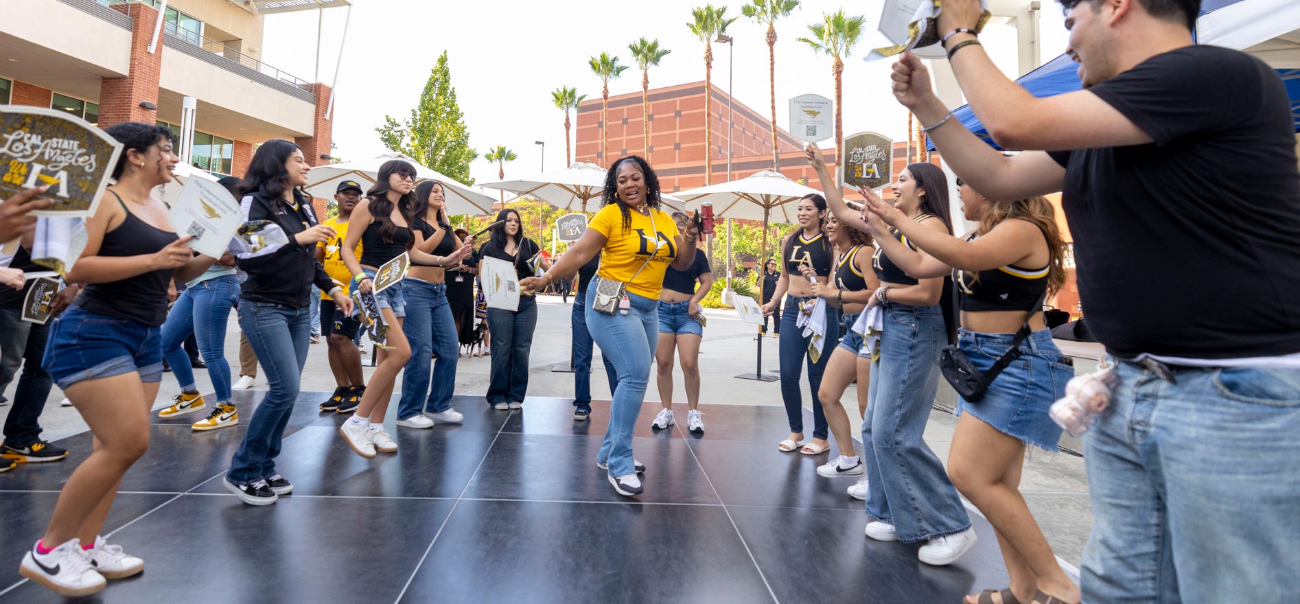 Cal State LA students and staff dance together in the University-Student Union plaza during the 2025 Community Celebration, waving Cal State LA spirit signs and wearing campus colors.