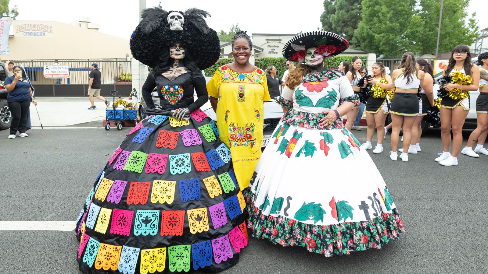 Cal State LA President Berenecea Johnson Eanes stands with two participants dressed in colorful Día de los Muertos costumes during a community parade.