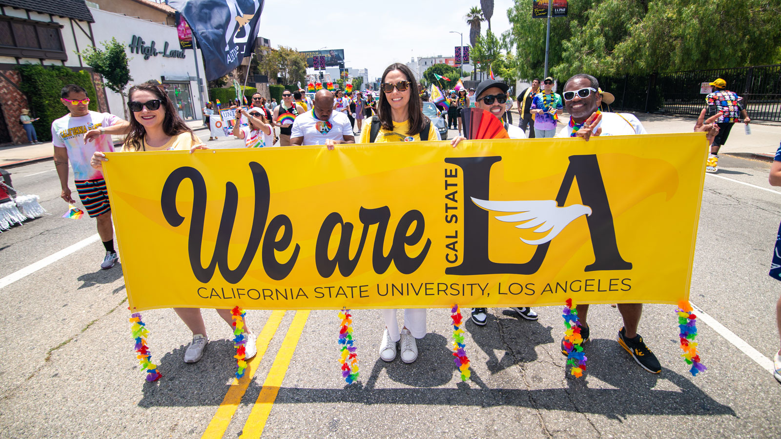 Cal State LA students and staff march in a community parade holding a bright yellow “We are LA” banner, celebrating school pride and inclusivity.