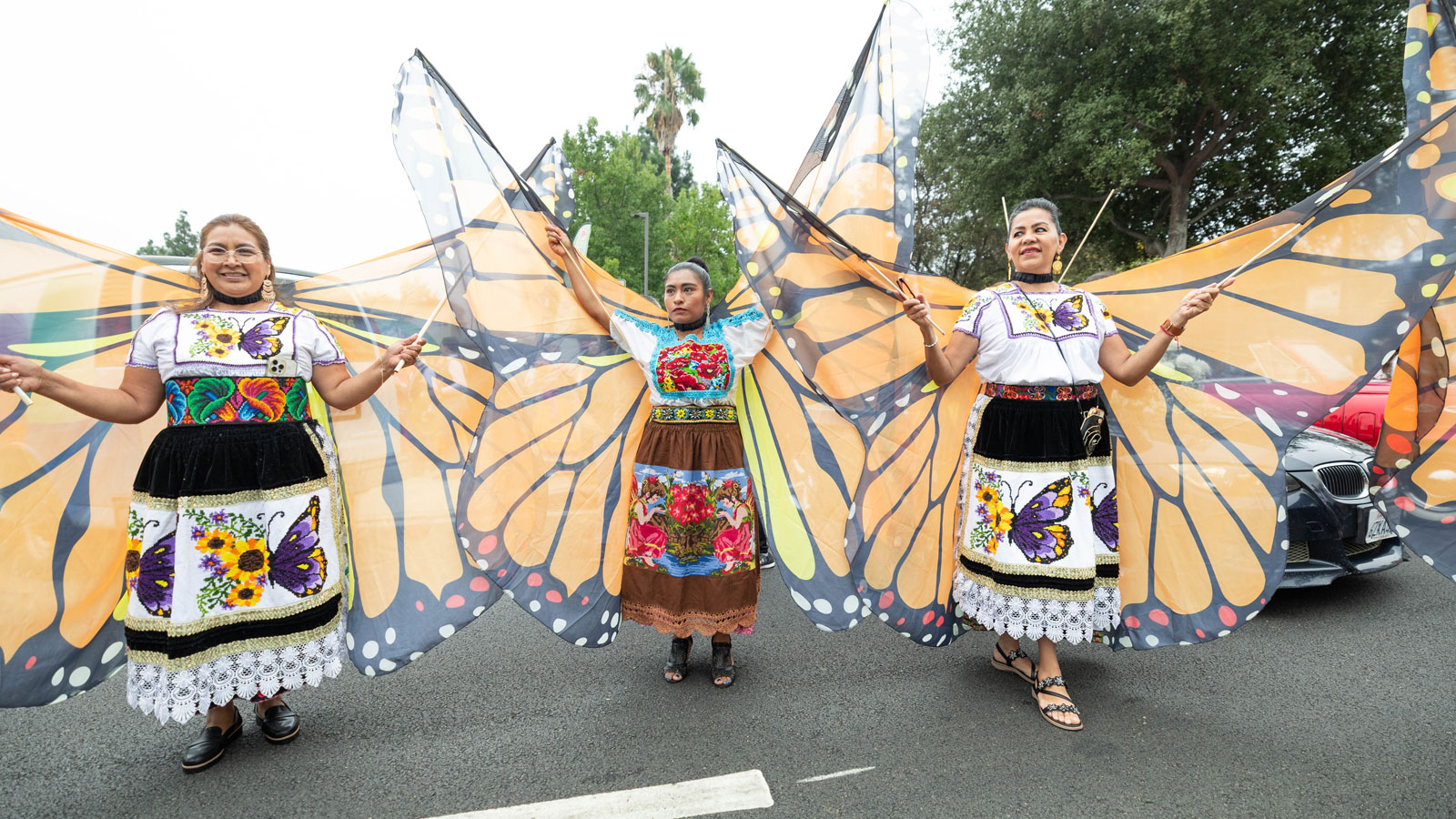 Parade participants dressed in traditional Mexican attire with large monarch butterfly wings celebrate culture and community during a Los Angeles event.