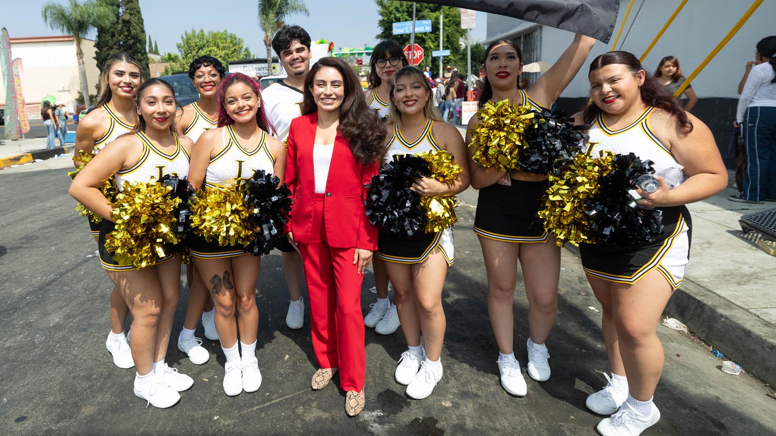 A person in a red suit poses with Cal State LA cheer team members holding pom-poms during a community parade.