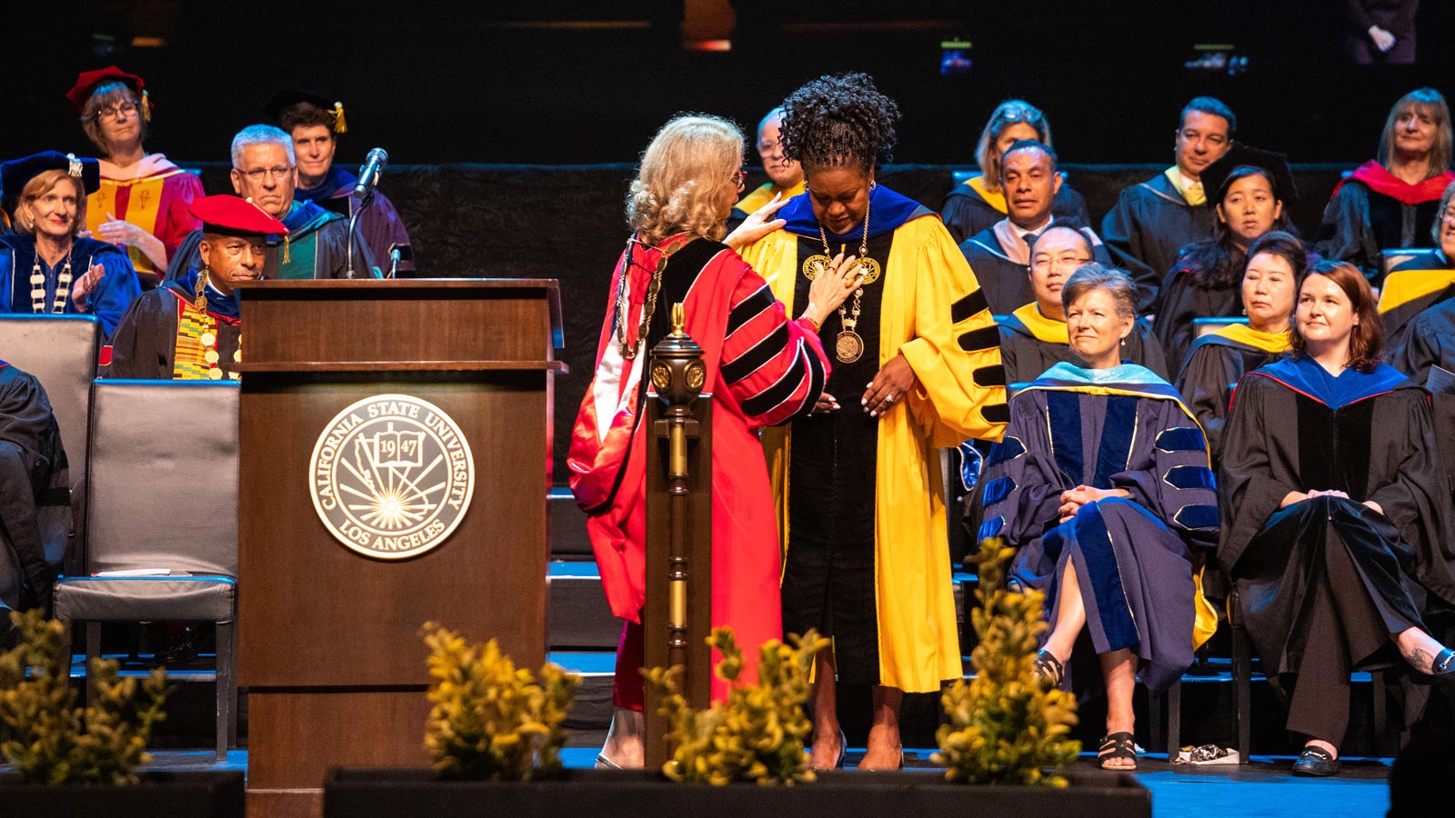 Cal State LA President Berenecea Johnson Eanes receives the presidential medallion on stage during the 2025 Investiture ceremony, surrounded by faculty in academic regalia.