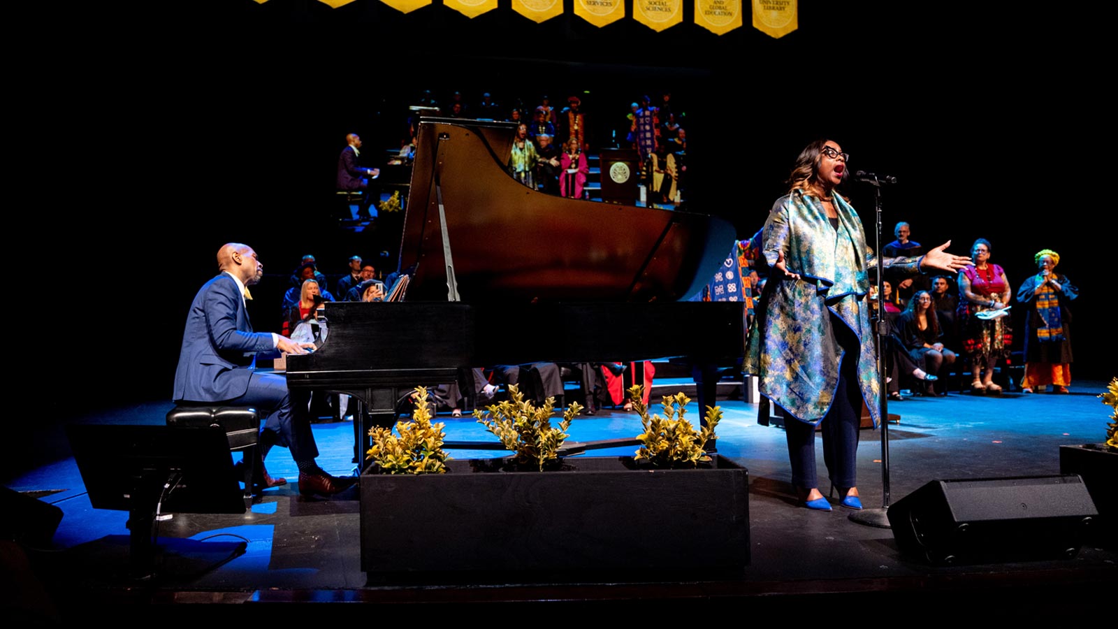 A pianist and vocalist perform on stage during the Cal State LA Investiture of President Berenecea Johnson Eanes 2025, with faculty and guests watching from behind.