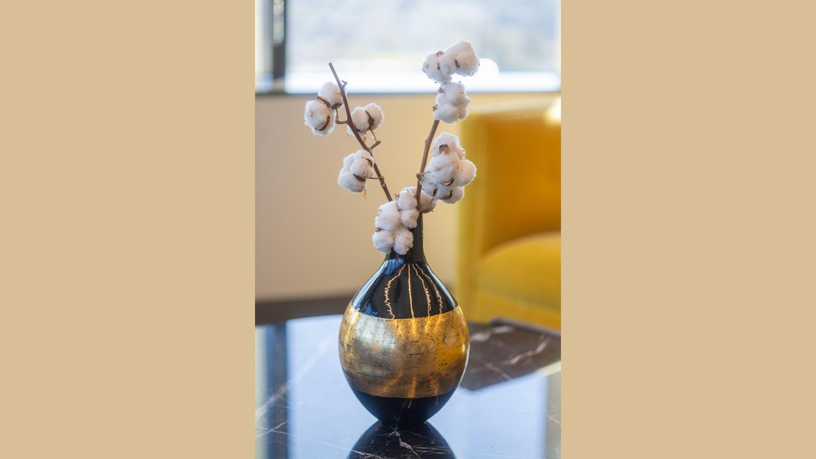 A black and gold vase holding cotton stems sits on a marble table near a yellow chair in an office at Cal State LA.