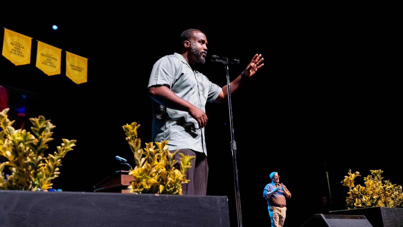 Performer speaks on stage during the Cal State LA Investiture of President Berenecea Johnson Eanes 2025, with college banners and a sign language interpreter visible in the background.