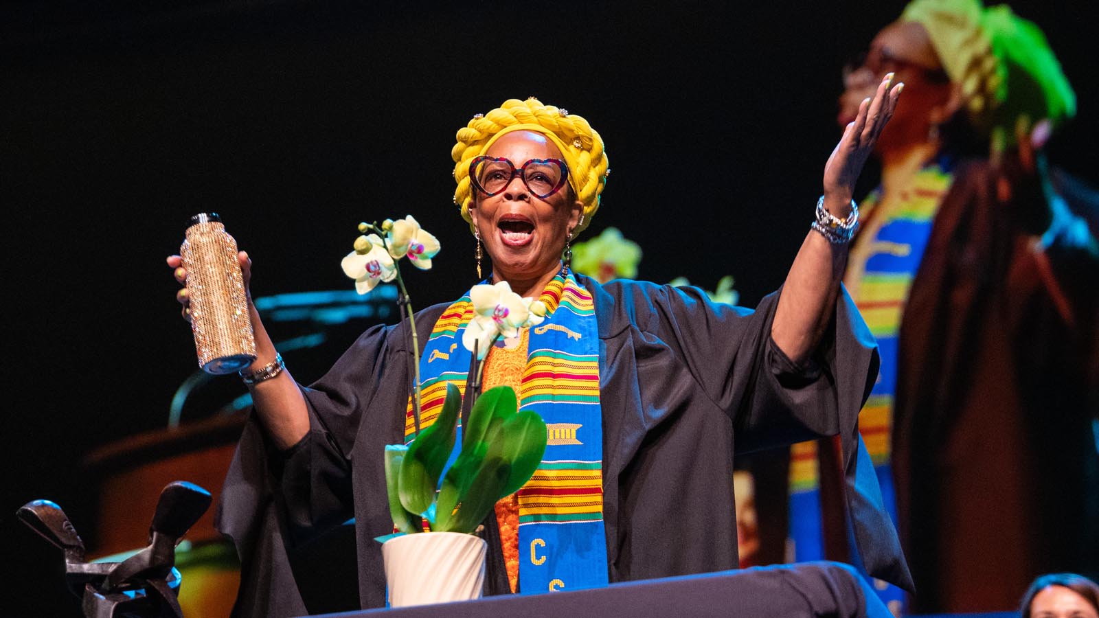 Performer wearing a bright yellow headwrap and robe gestures to the audience during the Cal State LA Investiture of President Berenecea Johnson Eanes 2025.