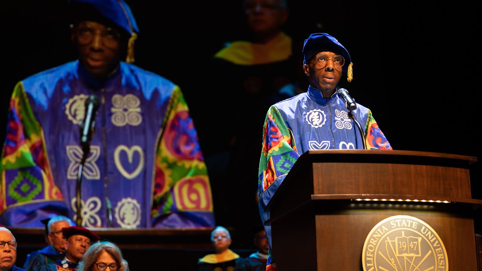 Speaker in colorful academic regalia delivers remarks from the Cal State LA podium at the Investiture of President Berenecea Johnson Eanes 2025.