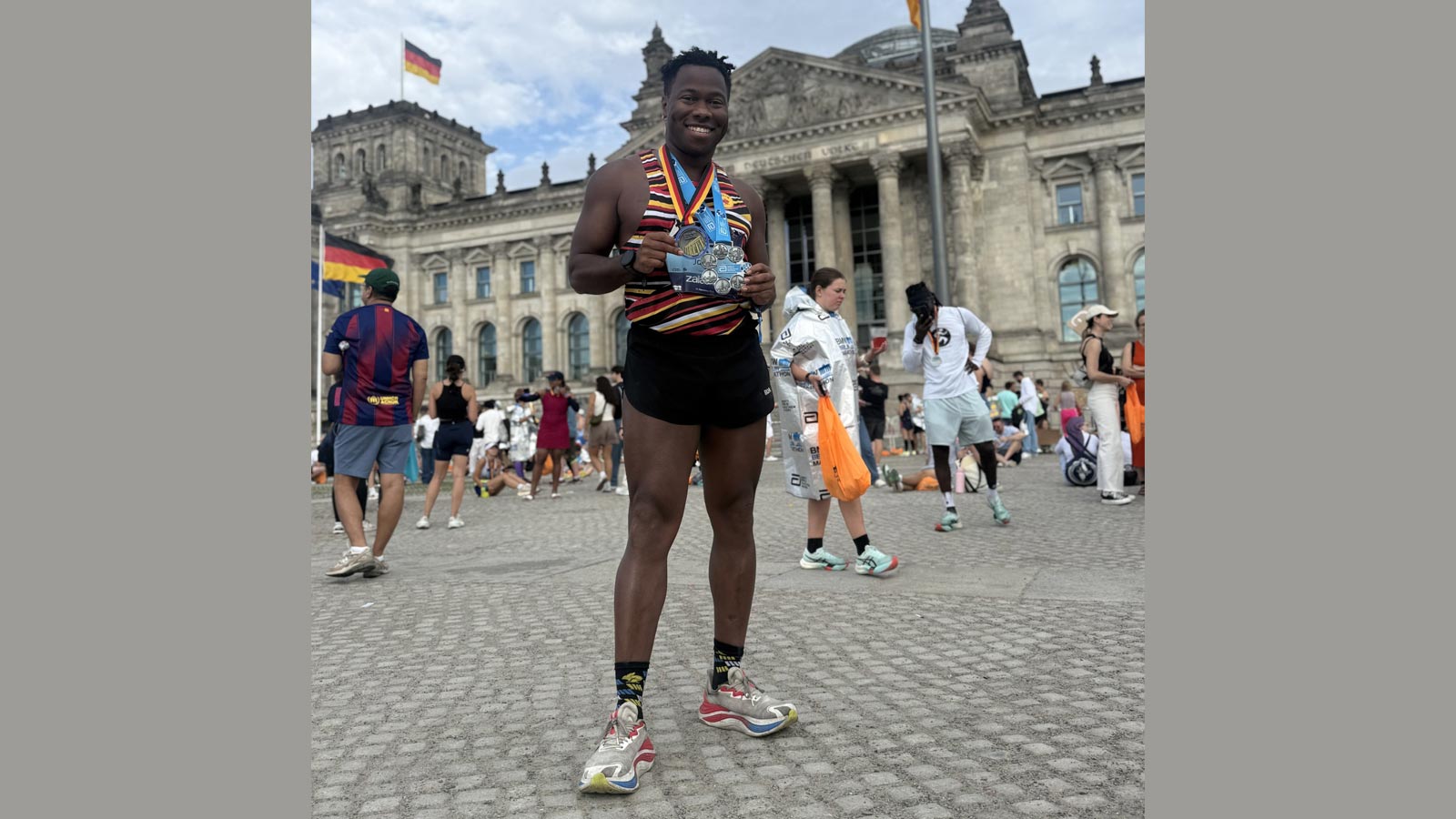 Cal State LA alumnus JT Chestnut stands proudly outside the Reichstag in Berlin, holding marathon medals after completing the Abbott World Marathon Majors.