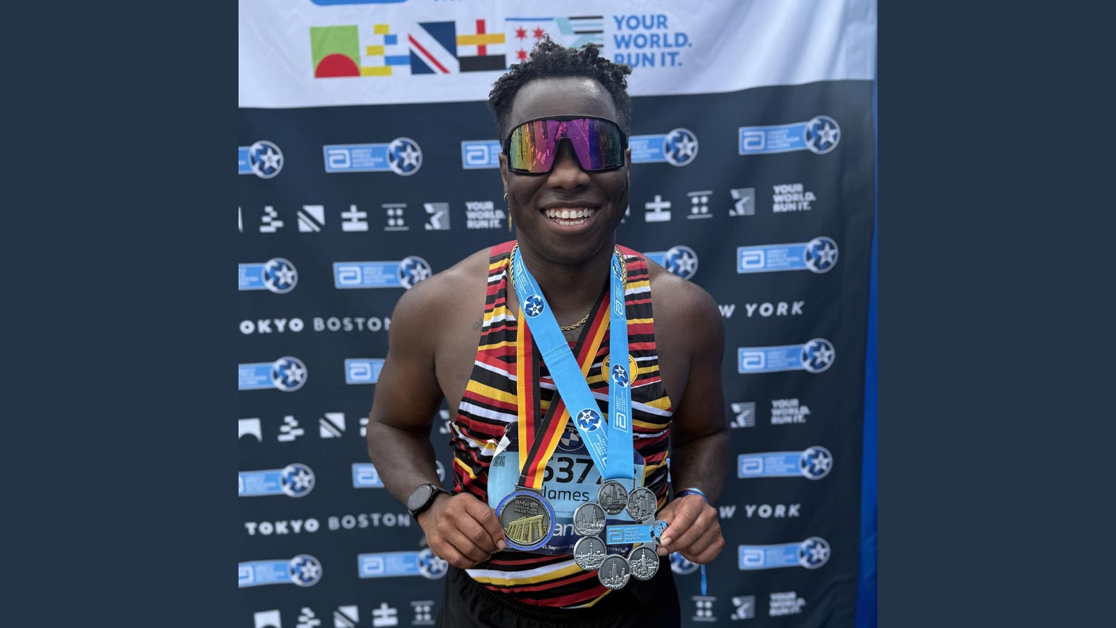 Cal State LA alumnus JT Chestnut poses with Abbott World Marathon Majors medals after completing the Berlin Marathon, smiling in front of the event backdrop.