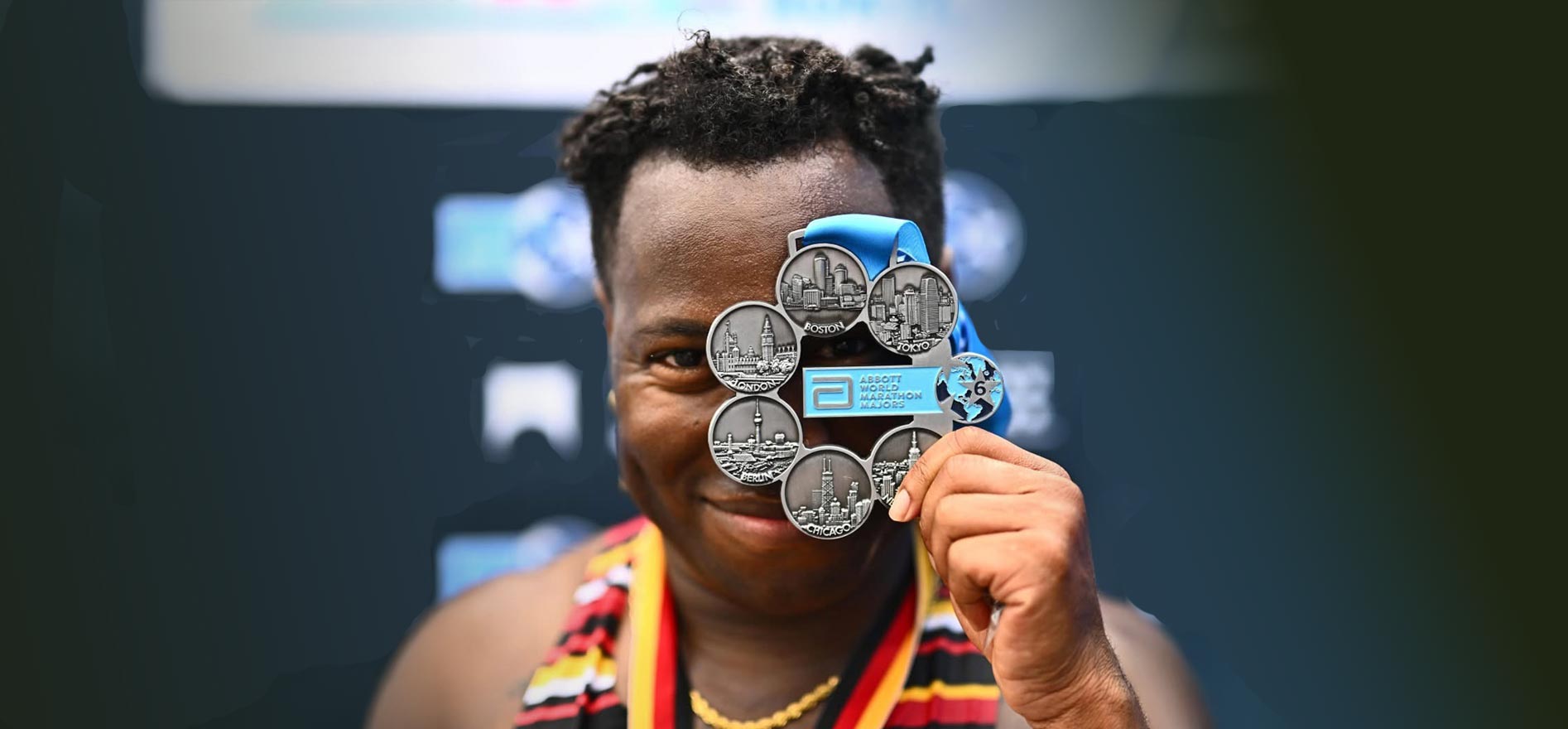 Cal State LA alumnus JT Chestnut holds up a World Marathon Majors medal in front of their face after completing the Abbott World Marathon series.