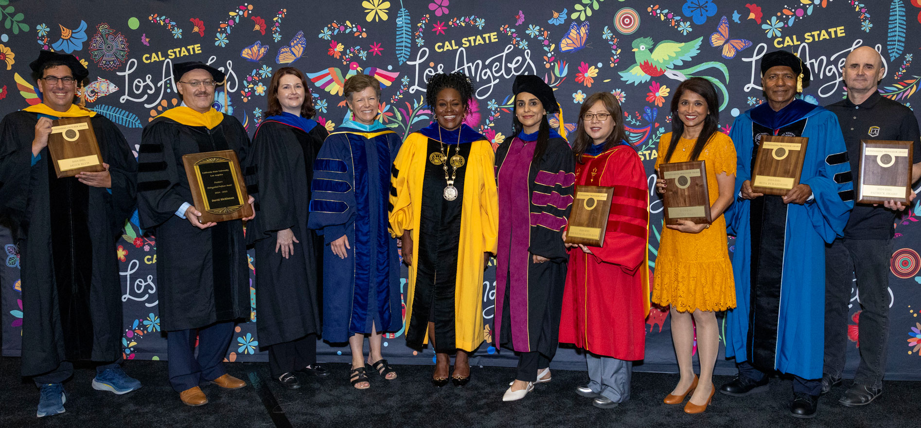 Cal State LA President Berenecea Johnson Eanes stands with 2025 Outstanding Professor Award recipients and faculty honorees in academic regalia against a colorful Cal State LA backdrop.