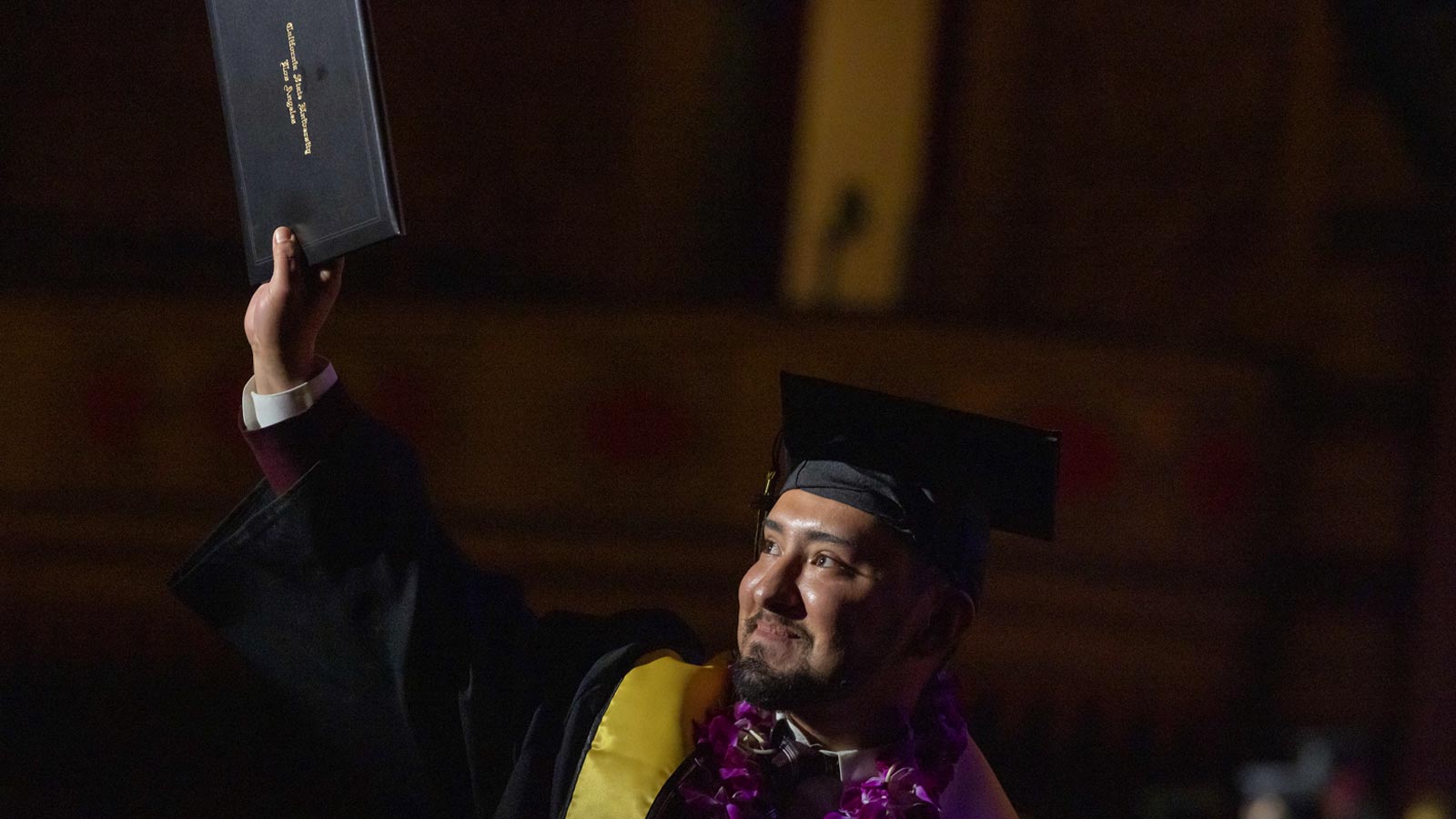 A Cal State LA graduate raises their diploma in celebration during the 2025 Commencement ceremony, symbolizing achievement and upward mobility.