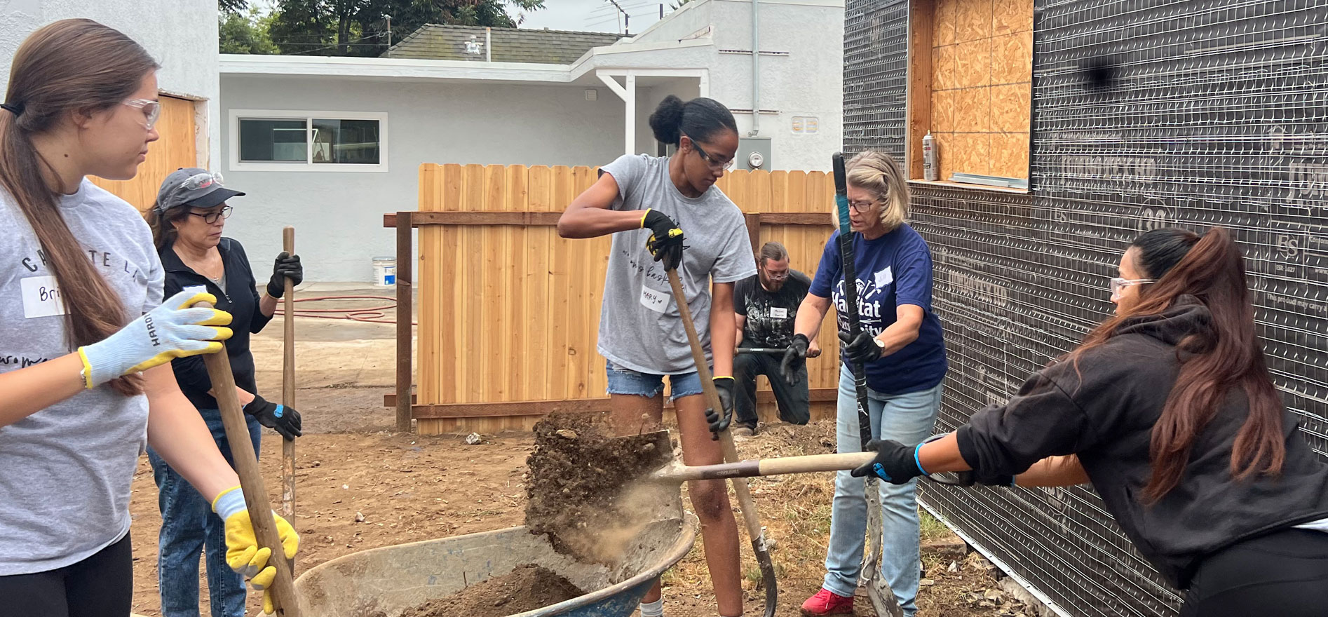 Cal State LA women’s basketball players work with Habitat for Humanity volunteers, shoveling dirt and preparing the foundation at a construction site.